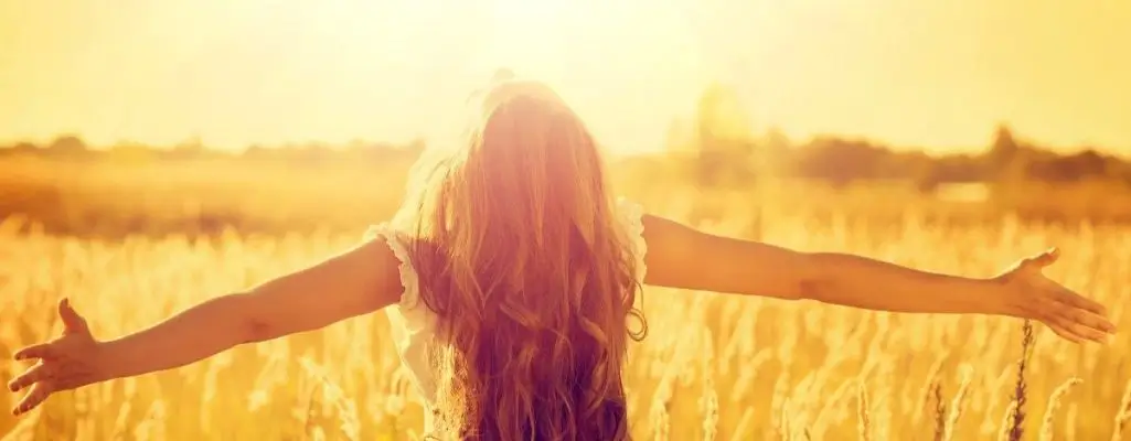 Obrazek wyróżniający do artykułu - mądre cytaty. Zdjęcie przedstawia osobę stojącą w polu pełnym wysokich traw, z rozłożonymi ramionami, twarzą skierowaną w stronę słońca. Osoba ta ma długie, rozpuszczone włosy, które swobodnie opadają na plecy. Scena jest oświetlona ciepłym, złotym światłem, co sugeruje wschód lub zachód słońca. Ogólny klimat obrazu to uczucie wolności, radości i jedności z naturą, wyrażające moment pełen spokoju i harmonii.