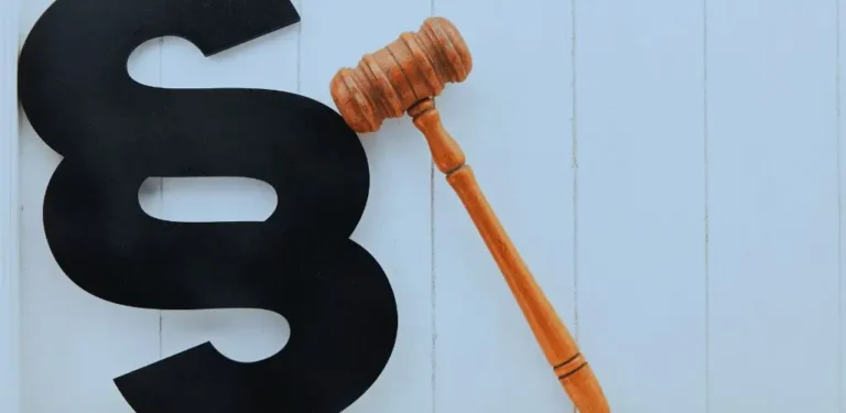 Obrazek wyróżniający do artykułu - co daje lekki stopień niepełnosprawności. Na zdjęciu widnieje duży symbol paragrafu w kolorze czarnym, ustawiony na jasnym, drewnianym tle. Obok niego znajduje się drewniany młotek sędziowski, będący symbolem wymiaru sprawiedliwości i decyzji prawnych. Obraz może odnosić się do tematyki związanej z prawem, regulacjami prawnymi lub procedurami legislacyjnymi. Proste, kontrastowe elementy przyciągają uwagę, a kolorystyka nadaje całości minimalistyczny i profesjonalny charakter.