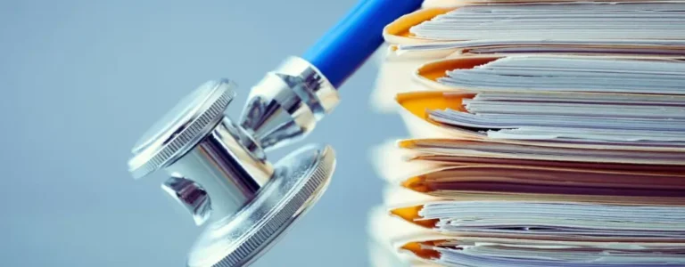 Obrazek wyróżniający do artykułu - Orzeczenie o niepełnosprawności. Na zdjęciu widać stos dokumentów, które są ułożone w schludny stos, a na nich oparty jest stetoskop. Obraz przedstawia połączenie tematyki medycznej z formalnymi dokumentami, co sugeruje związki między zdrowiem a dokumentacją prawną lub administracyjną, taką jak orzeczenia lekarskie czy dokumentacja związana z opieką zdrowotną. Stetoskop z metalową głowicą i niebieskim przewodem dodaje element medyczny, co może nawiązywać do formalnych procedur oceny zdrowia lub diagnostyki w kontekście prawnym.